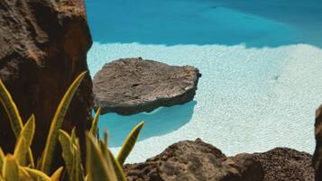 Una piscina azul cristalina rodeada de rocas y plantas.