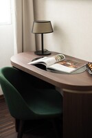 A small, curved wooden table with a lamp and a magazine. A green chair is positioned in front of the table.