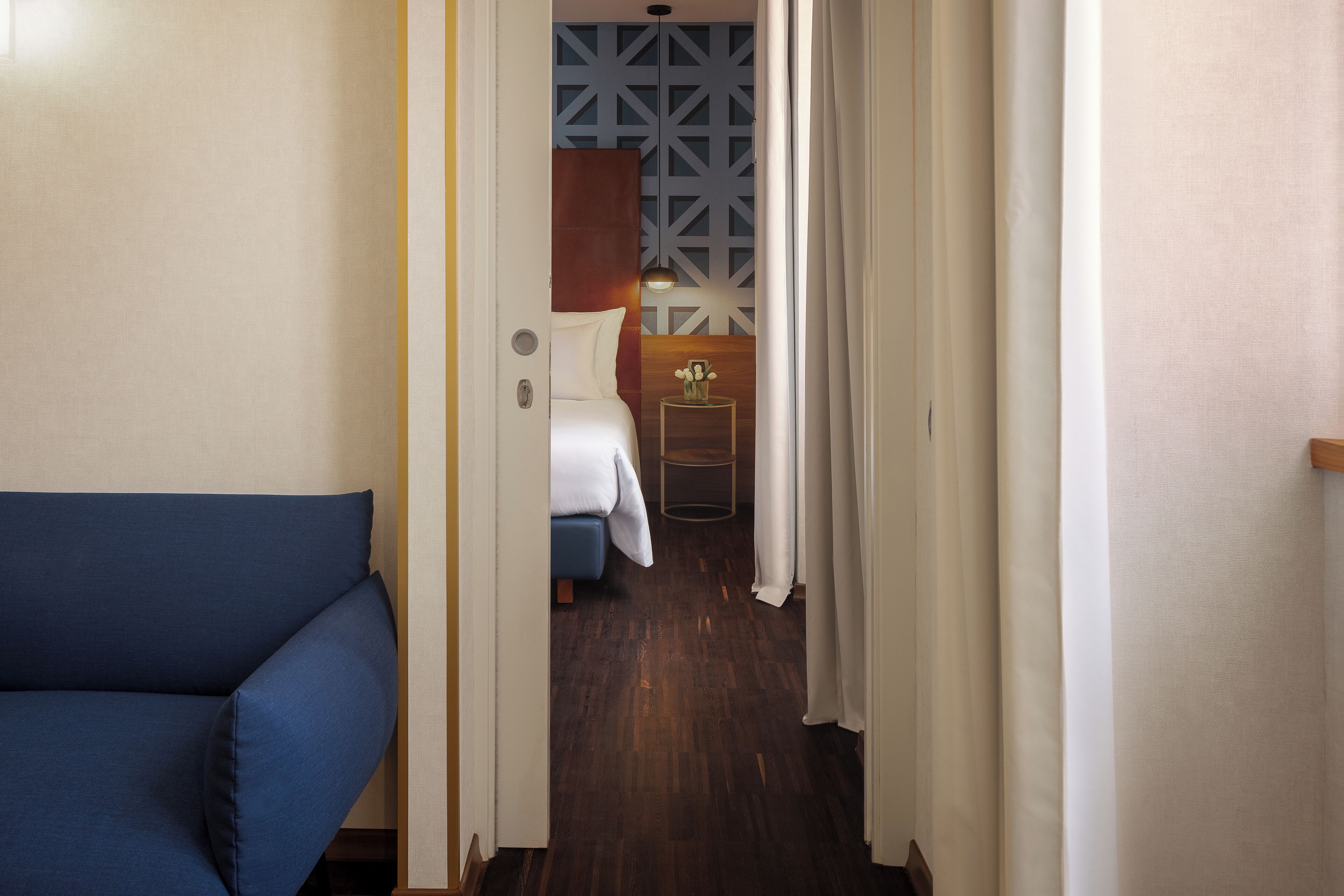 Un couloir étroit mène à une chambre à coucher qui contient un lit, une petite table avec un vase et un canapé bleu.