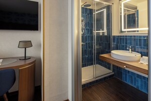Un bagno moderno con cabina doccia in vetro, lavabo rotondo e televisore a parete.