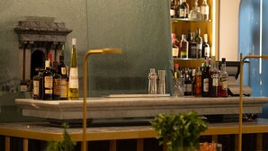 Zona de bar con mostrador de mármol, estantes llenos de botellas de licores y una pared decorativa.