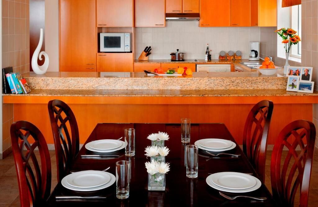 A kitchen with wooden cabinets, a microwave, and a dining area with a table set for four.