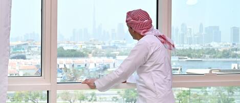 A person in traditional attire standing by a window with a cityscape view.