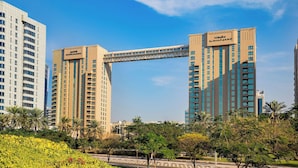 Een hoog hotel met een opvallende, gebogen brug die twee torens verbindt, omgeven door weelderige begroeiing en palmbomen.