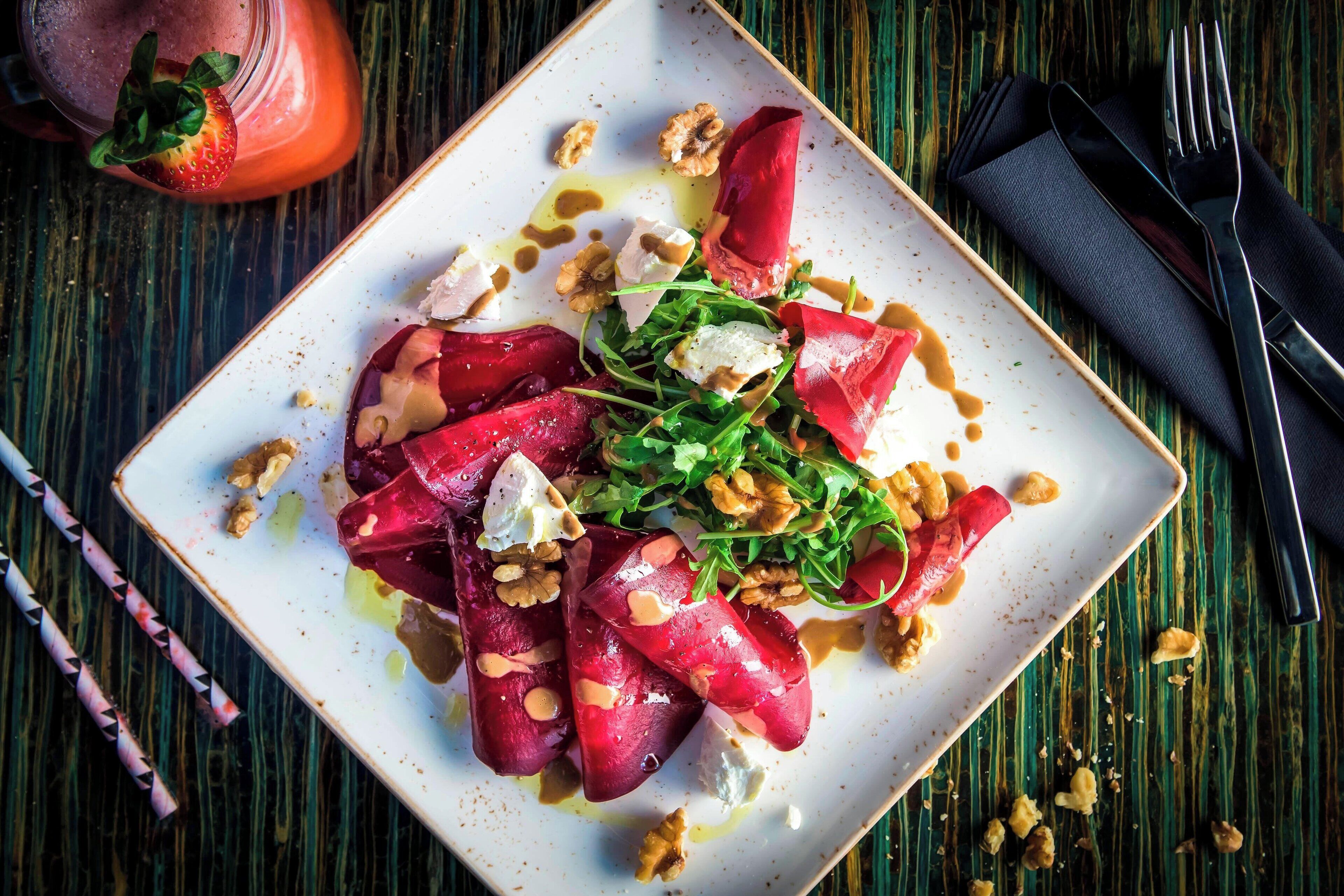 A square plate with a salad of beets, walnuts, and cheese on a wooden table.