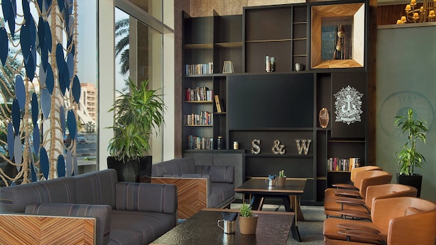 Een moderne zithoek met een bank, fauteuils, een salontafel en een boekenkast.