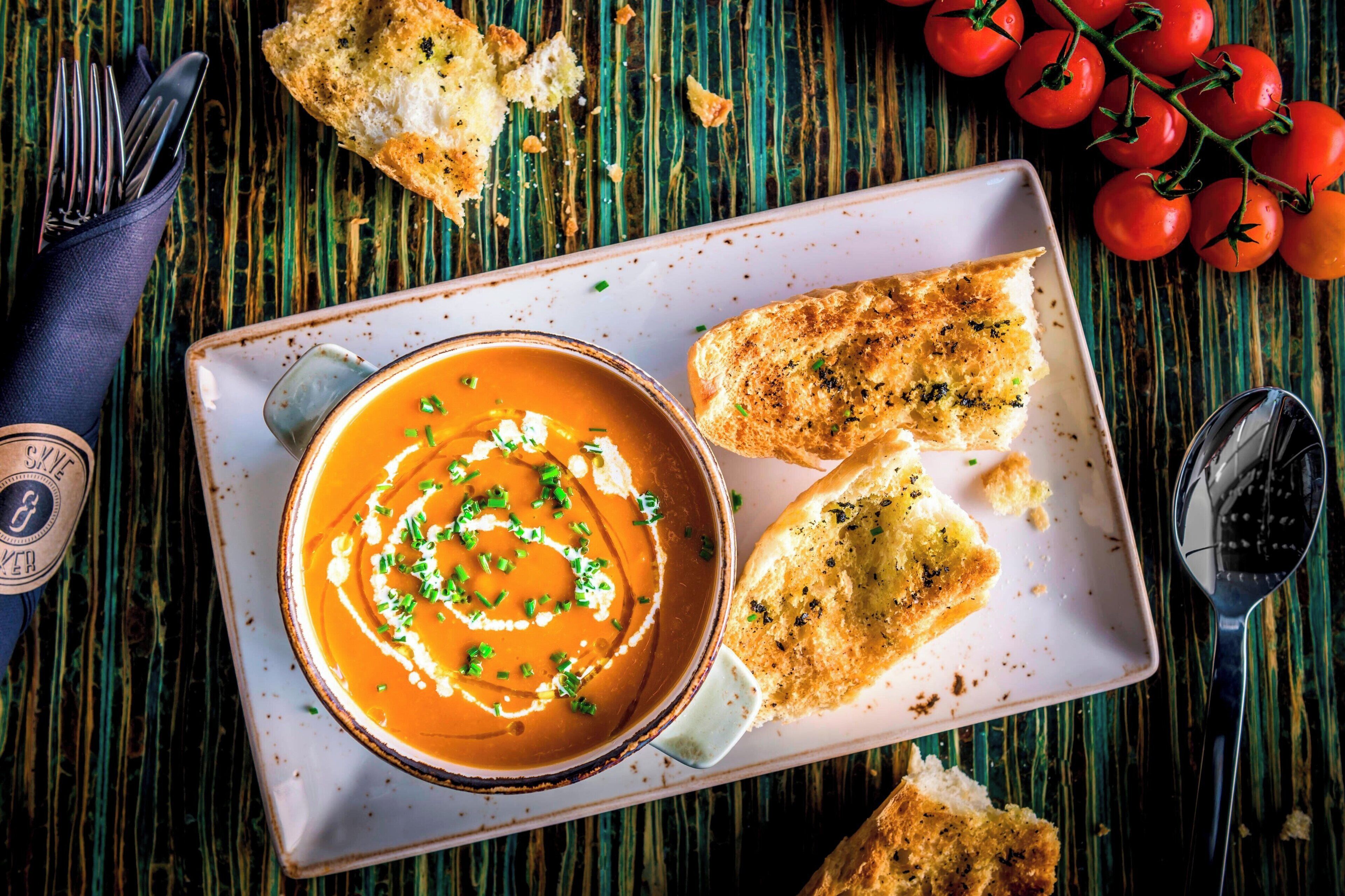 A bowl of soup with a swirl design, accompanied by pieces of bread and a spoon on a plate.