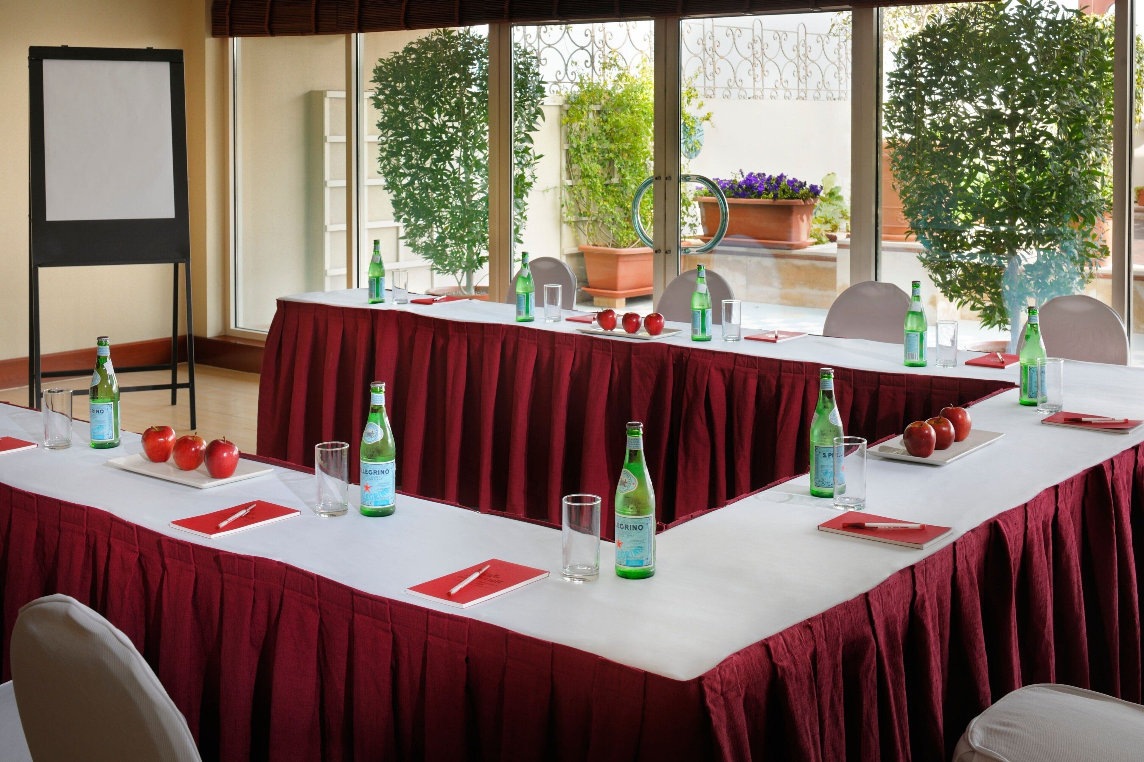 A conference room with a long table set for a meeting, adorned with red tablecloths, green bottles, and apples.