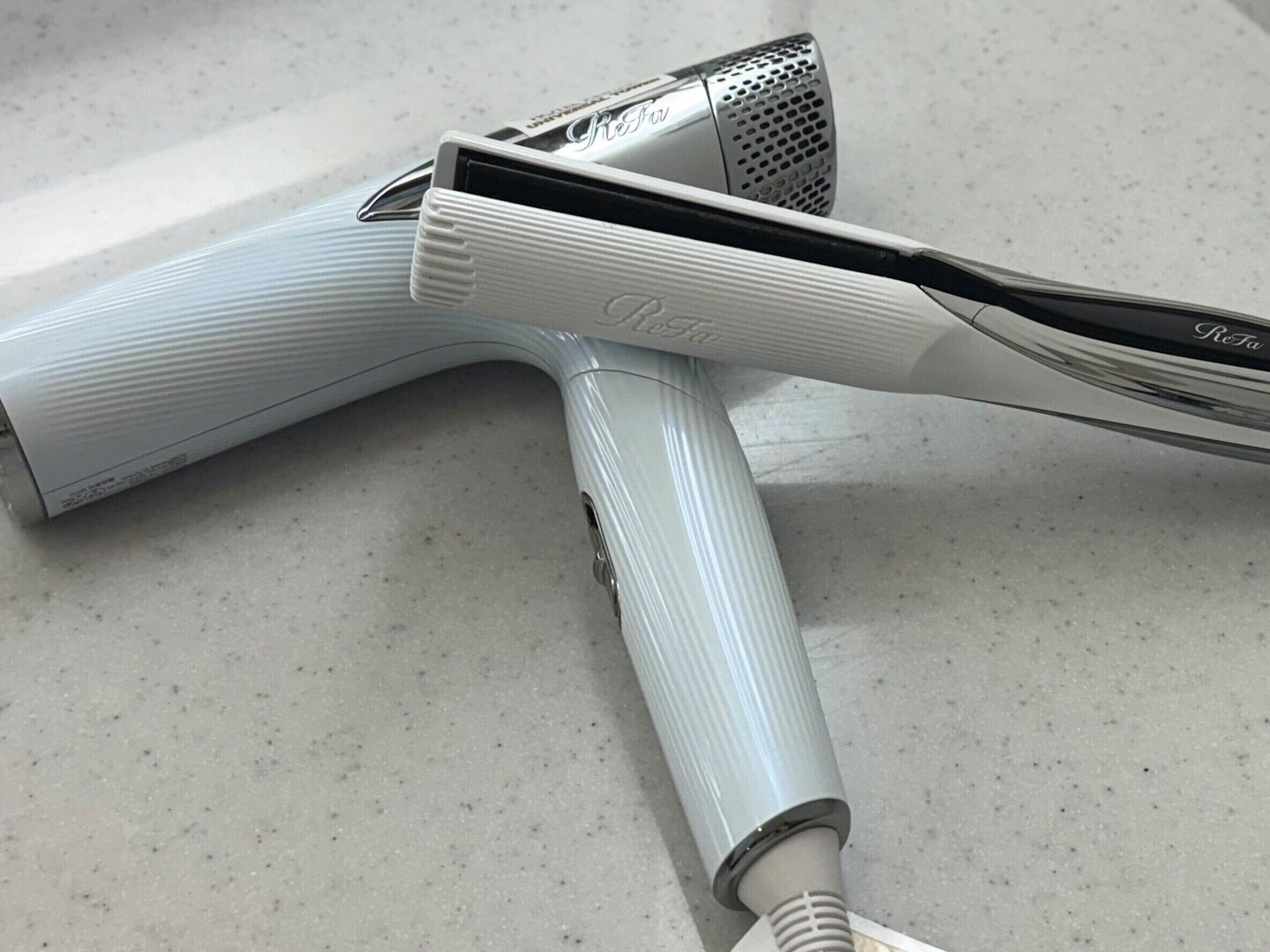 A hairdryer with a metallic nozzle and a white handle with the brand name "Reva" visible.