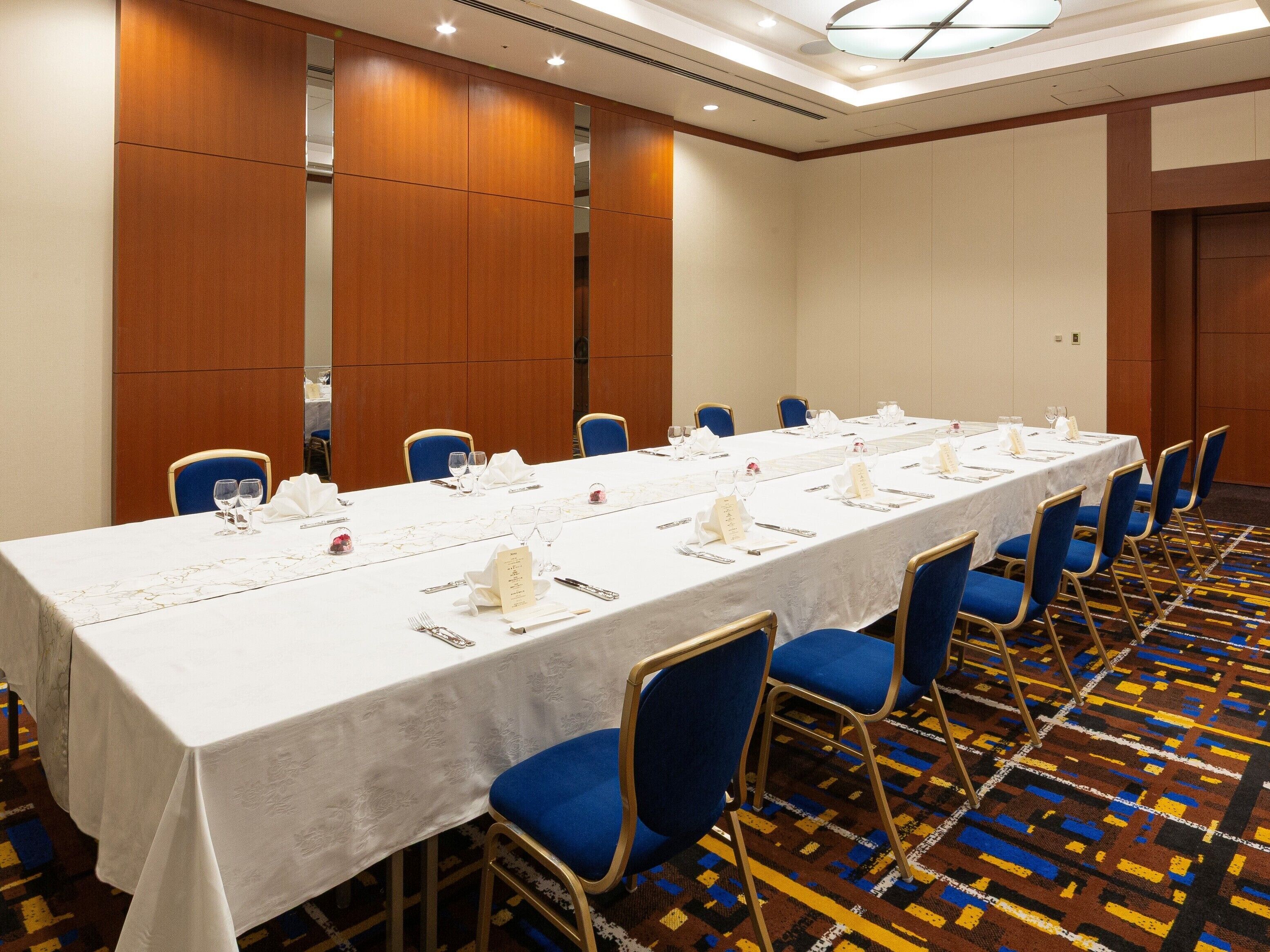 Un salón de conferencias con una larga mesa, sillas azules y una alfombra estampada.