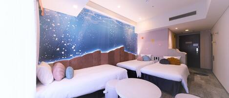 A hotel room with two beds, a sofa, a round table, and a wall mural.