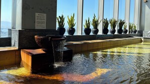 Zona de piscina con una cascada, plantas en macetas y vistas de la ciudad a través de amplios ventanales.