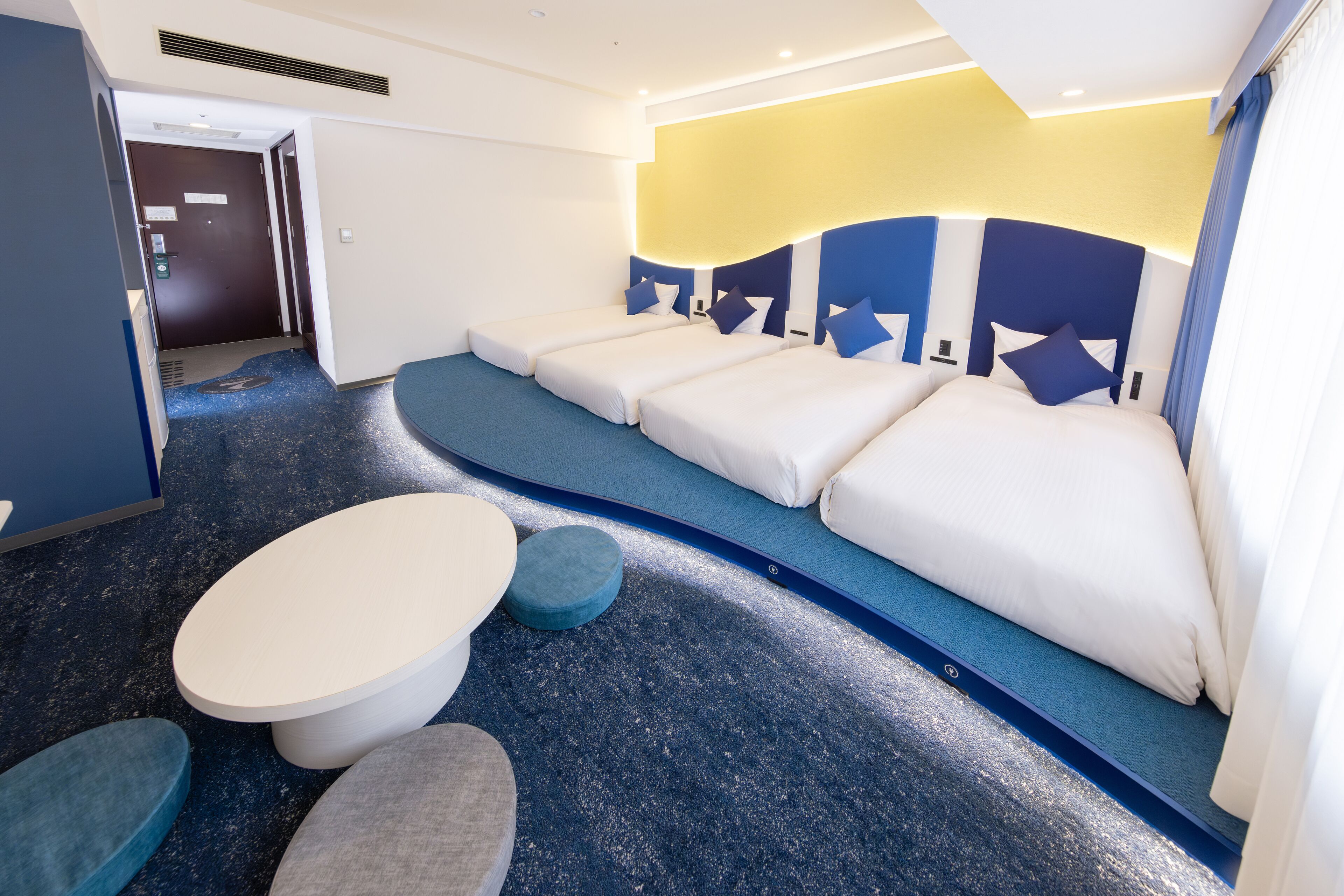 Ein Hotelzimmer mit blauem Teppich, einer Schlafcouch mit Kissen und einem kleinen runden Tisch.
