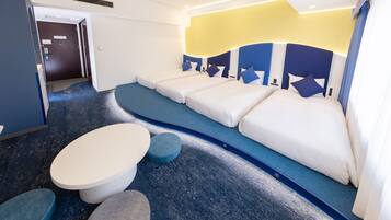 A hotel room with a blue carpet, a sofa bed with pillows, and a small round table.