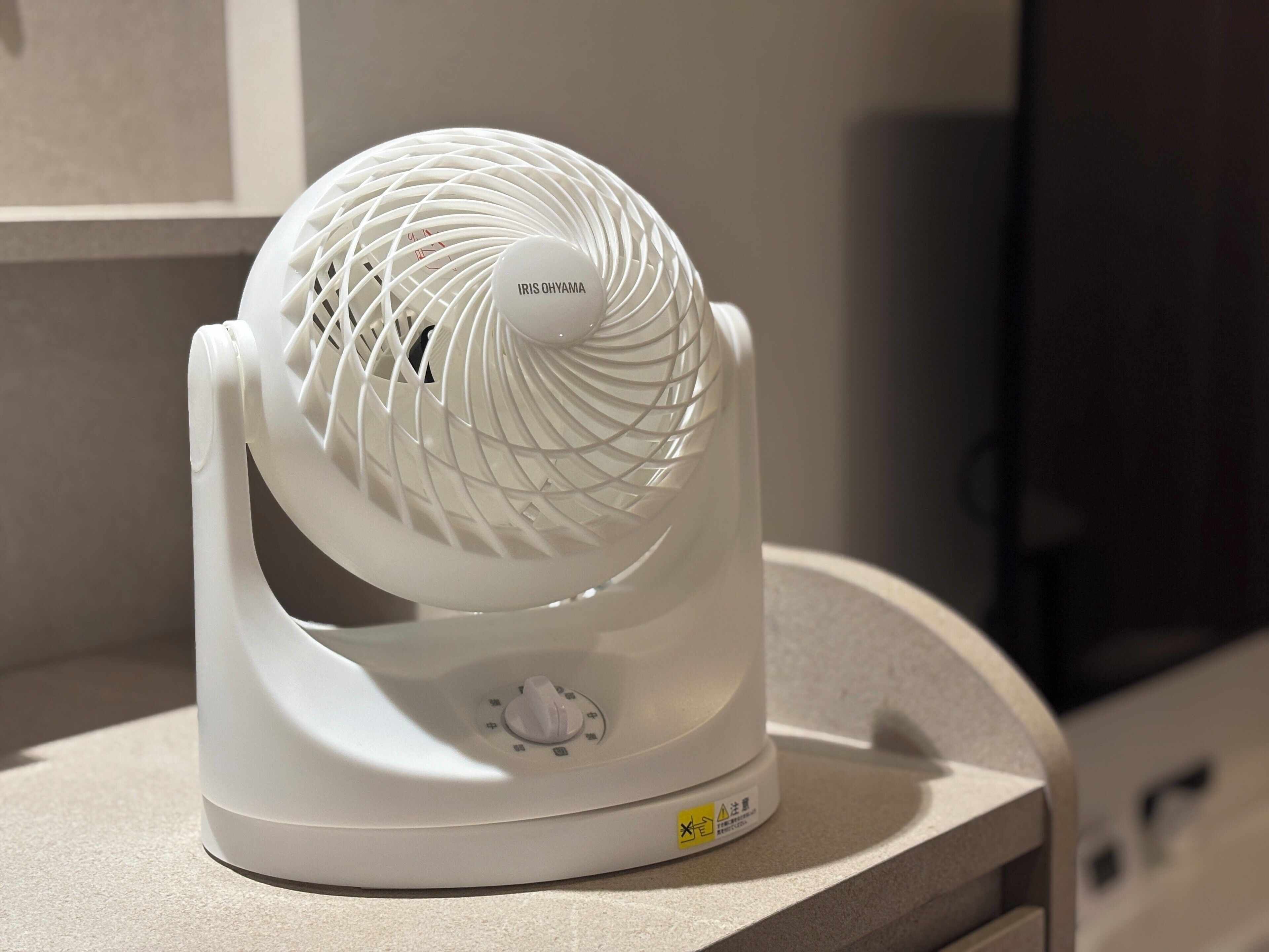 A white standing fan with a spherical design, placed on a countertop.