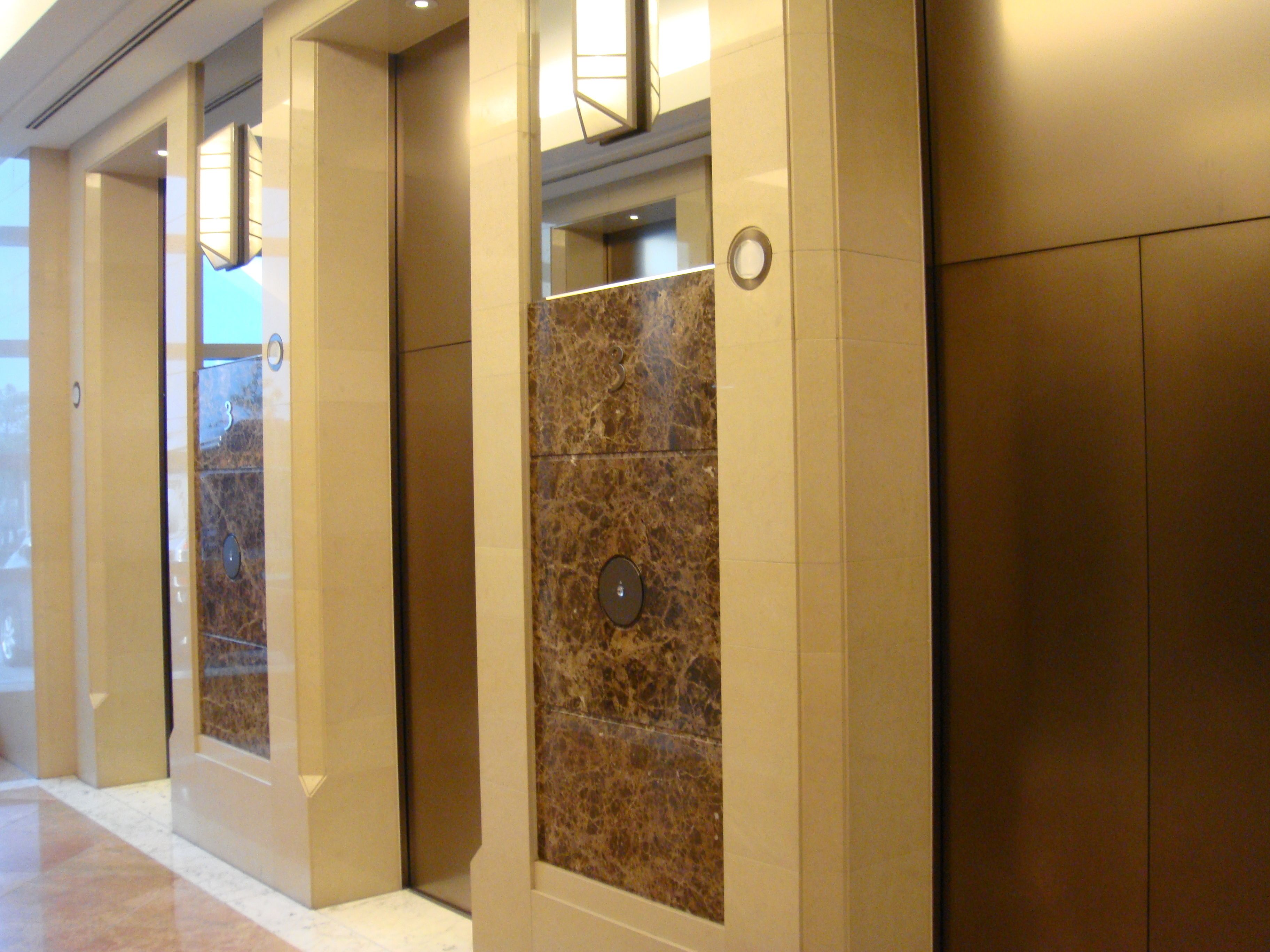 A corridor with marble walls and a polished floor, leading to elevators.