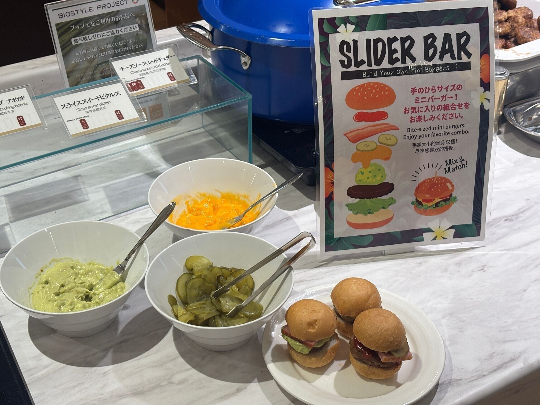 Un buffet proposant une variété de plats, notamment des mini-burgers, des cornichons et différentes sauces.