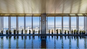 Una gran piscina interior con vistas a la ciudad, plantas en macetas y un reloj en la pared.
