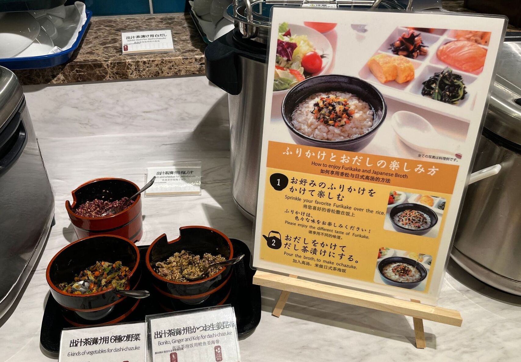 Mostra de menjar amb bols de rice i verdures, un cartell amb text japonès i un taulell amb safata blava.