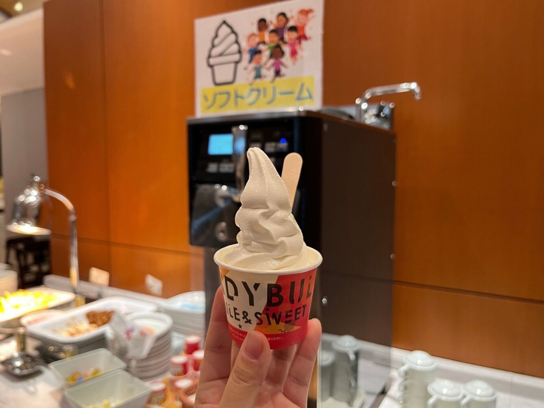 A hand holding a cup of soft-serve ice cream with 'DYBILE & SWEET' branding.