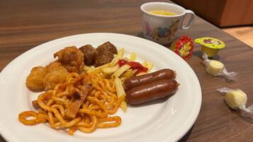 Ein Teller mit Essen, darunter Spaghetti, Fleischbällchen und Würstchen, dazu eine Tasse und einige verpackte Gegenstände auf dem Tisch.