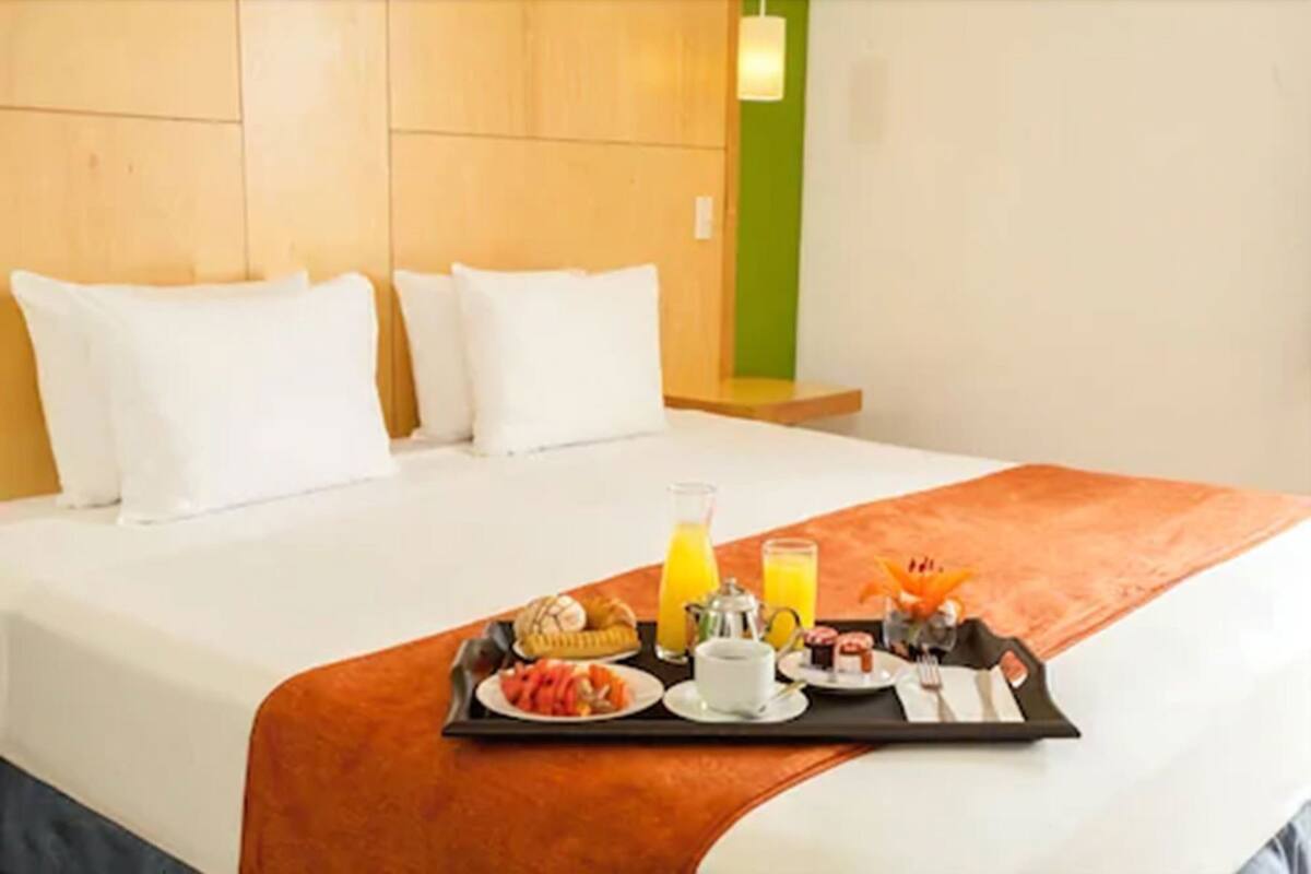 A hotel room with a neatly made bed, a tray with breakfast items, and a green accent wall.