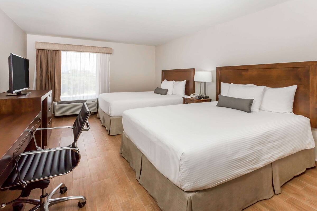 A hotel room with two beds, a desk with a chair, a TV, and a window with curtains.