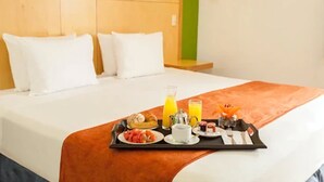 Une chambre d’hôtel avec un lit parfaitement fait, un plateau avec des articles pour le petit-déjeuner et un mur d’accent de couleur verte.