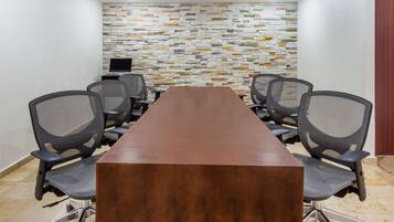 Un salón de conferencias con una larga mesa de madera, seis sillas de oficina y una pared con diseño de piedra.