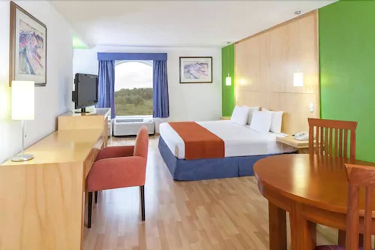 A hotel room with a bed, desk, chair, and a view of the outdoors.