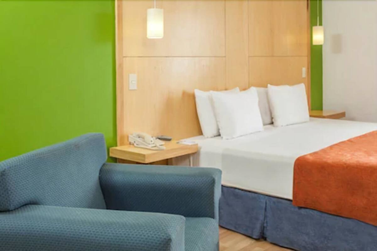 A hotel room with a bed, a nightstand, a blue armchair, and a green wall.