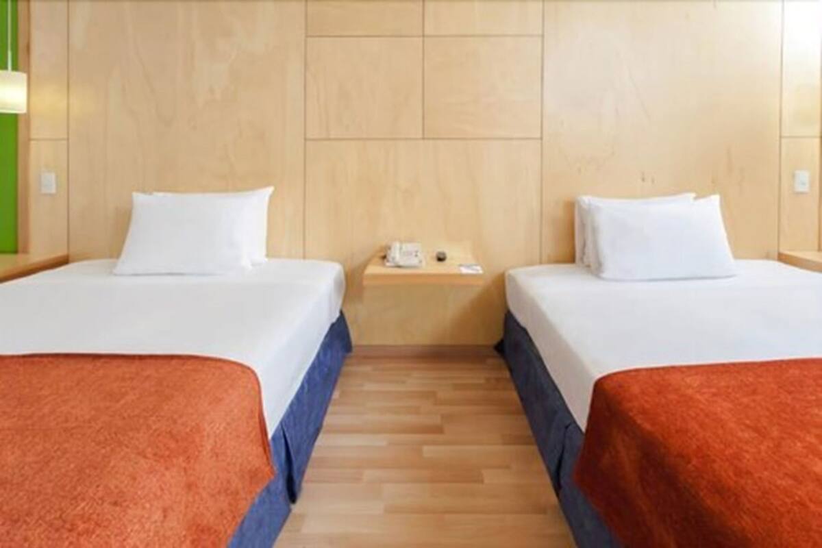 A hotel room with two beds, a wooden headboard, a nightstand with a phone, and a wooden floor.