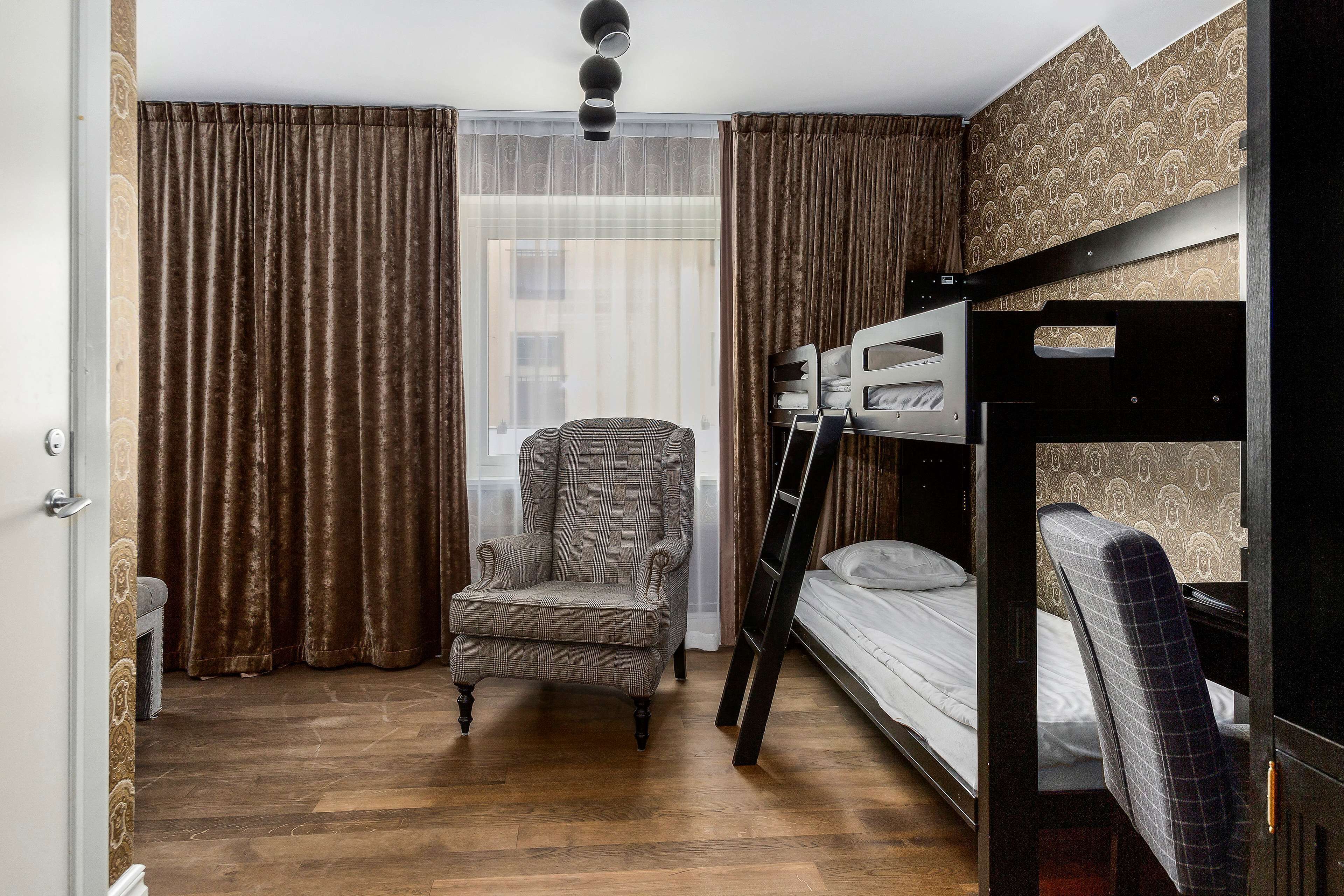 A room with a bunk bed, a chair, a desk, and a window with curtains.