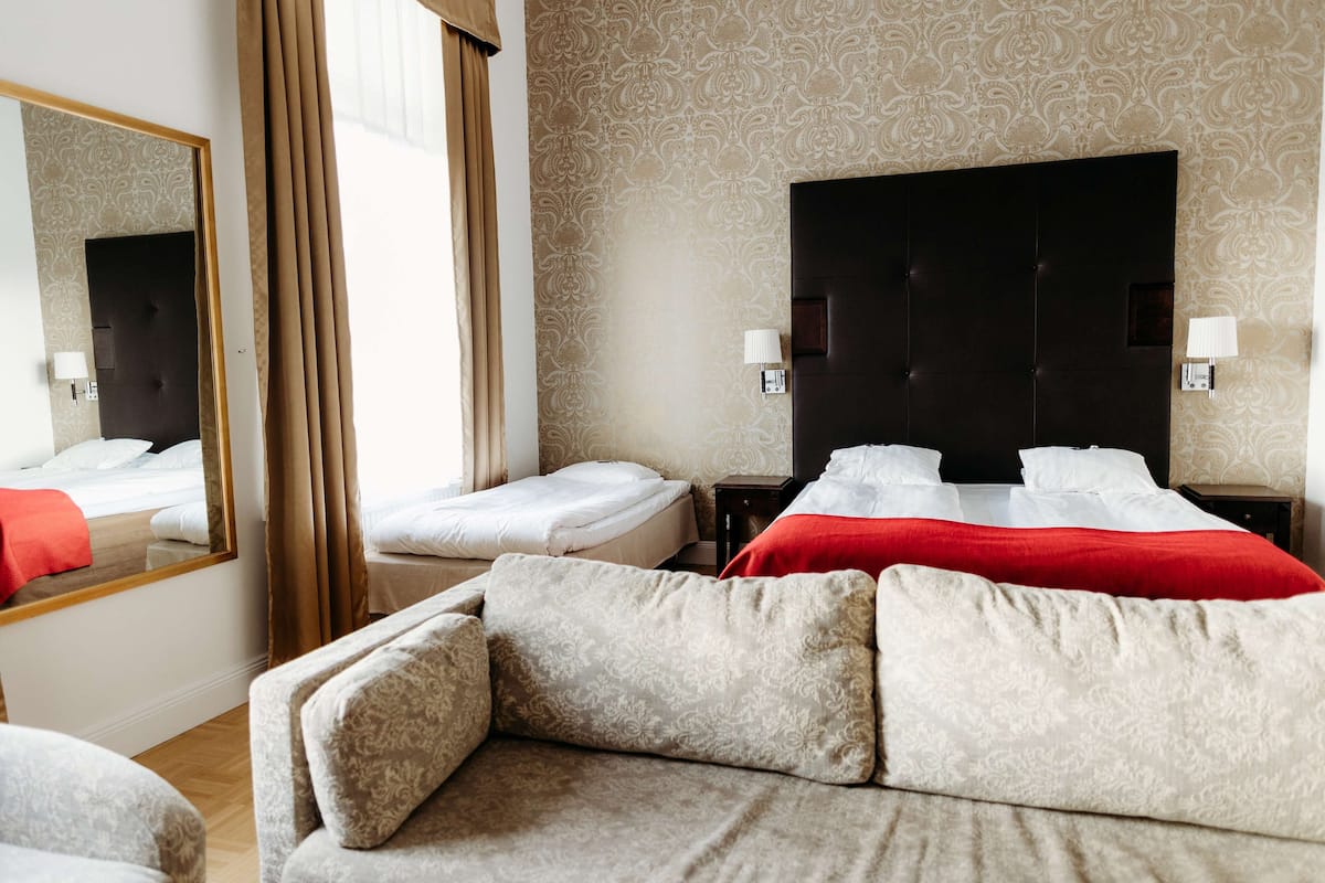 A hotel room with a large bed, a sofa, a mirror, and a patterned wall.