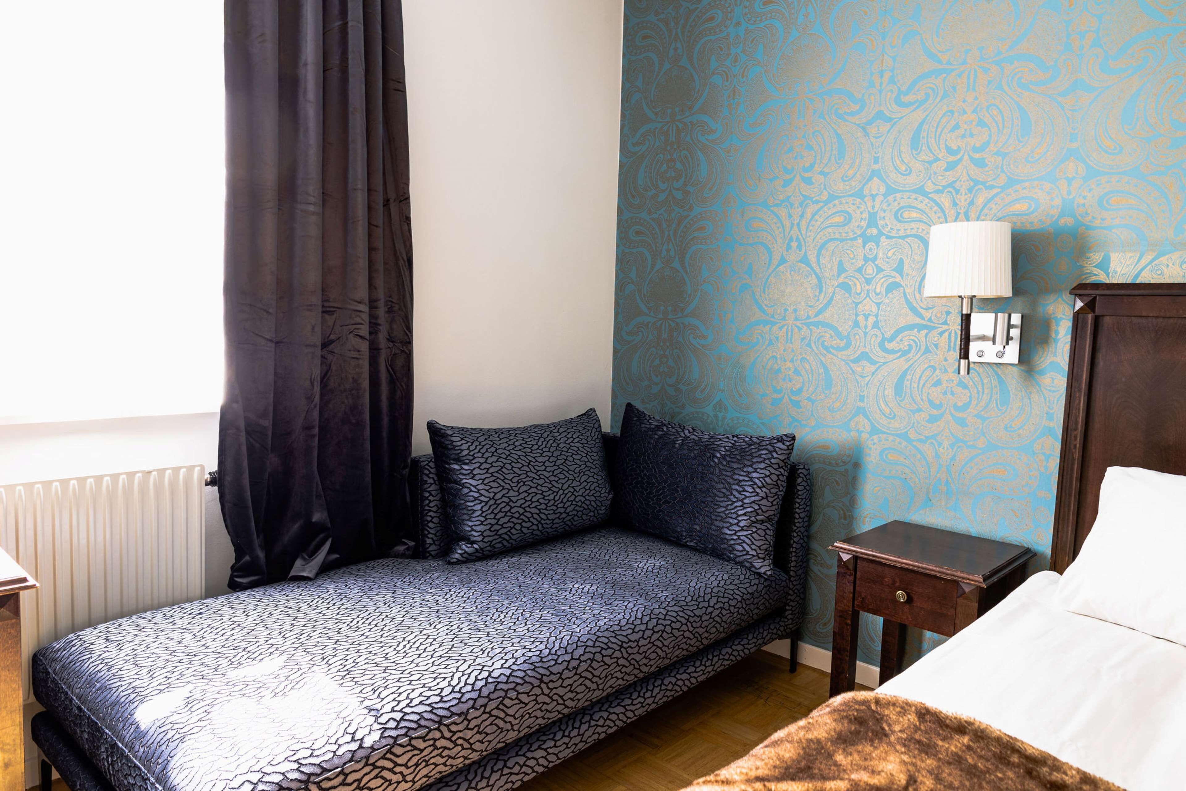 A bedroom with a bed, a nightstand, a lamp, and a window with curtains.