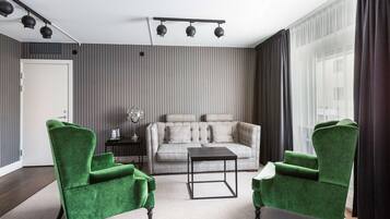 A modern living room with a grey sofa, two green armchairs, a coffee table, and a ceiling light fixture.