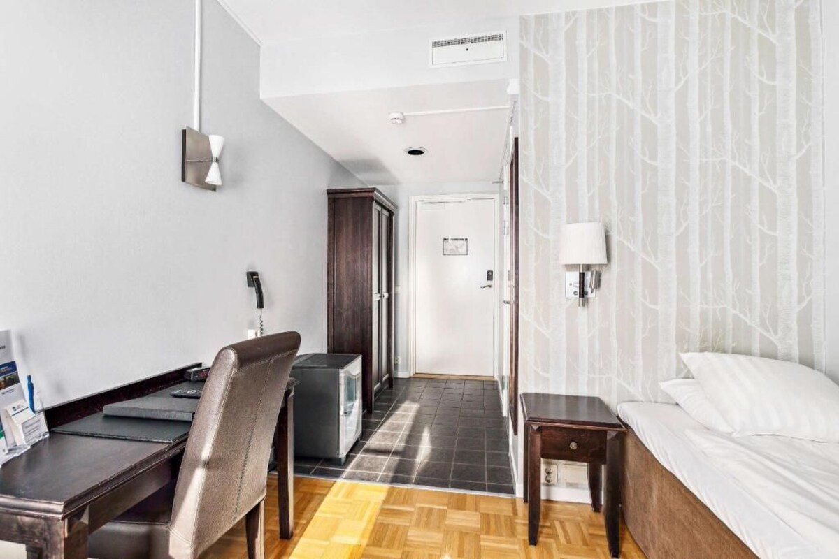 Een hotelkamer met een bureau, stoel, bed en een kledingkast.