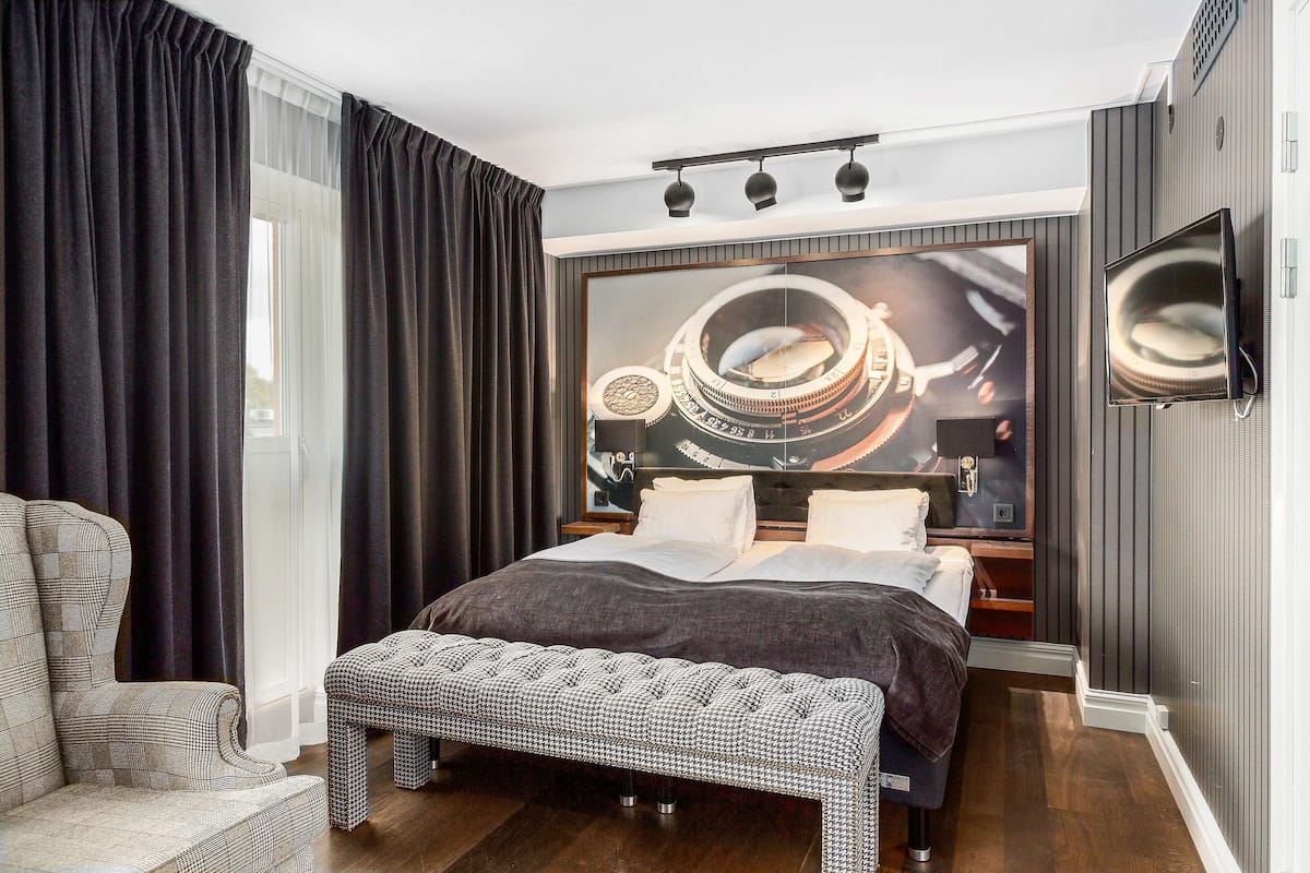 A modern bedroom with a large bed, a bench, a TV, and a wall-mounted artwork.