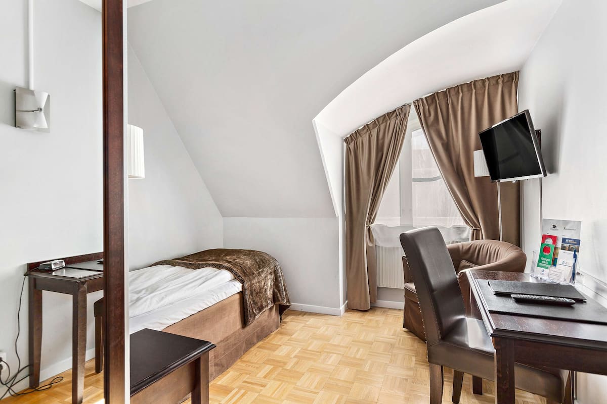 A compact hotel room with a bed, a desk, a chair, a TV, and a window with curtains.