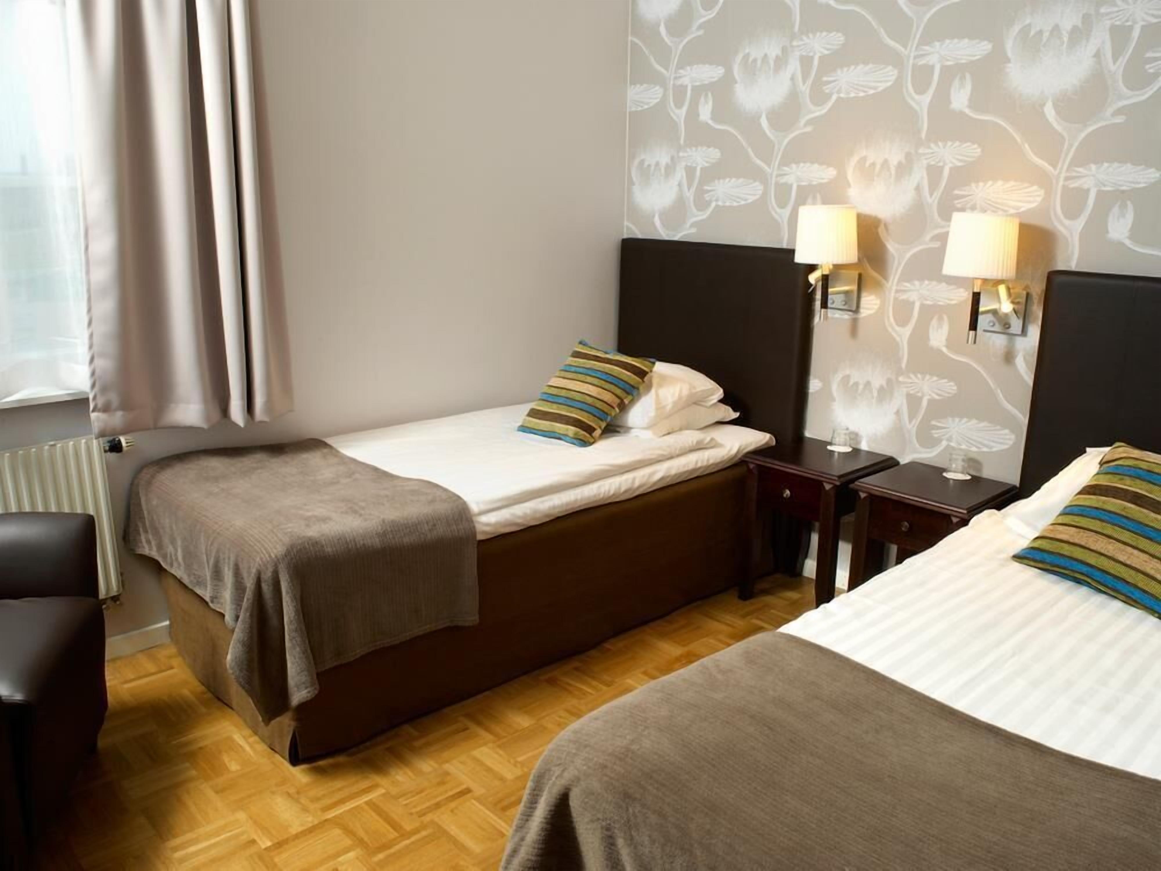A hotel room with two beds, a chair, a nightstand, and a lamp.