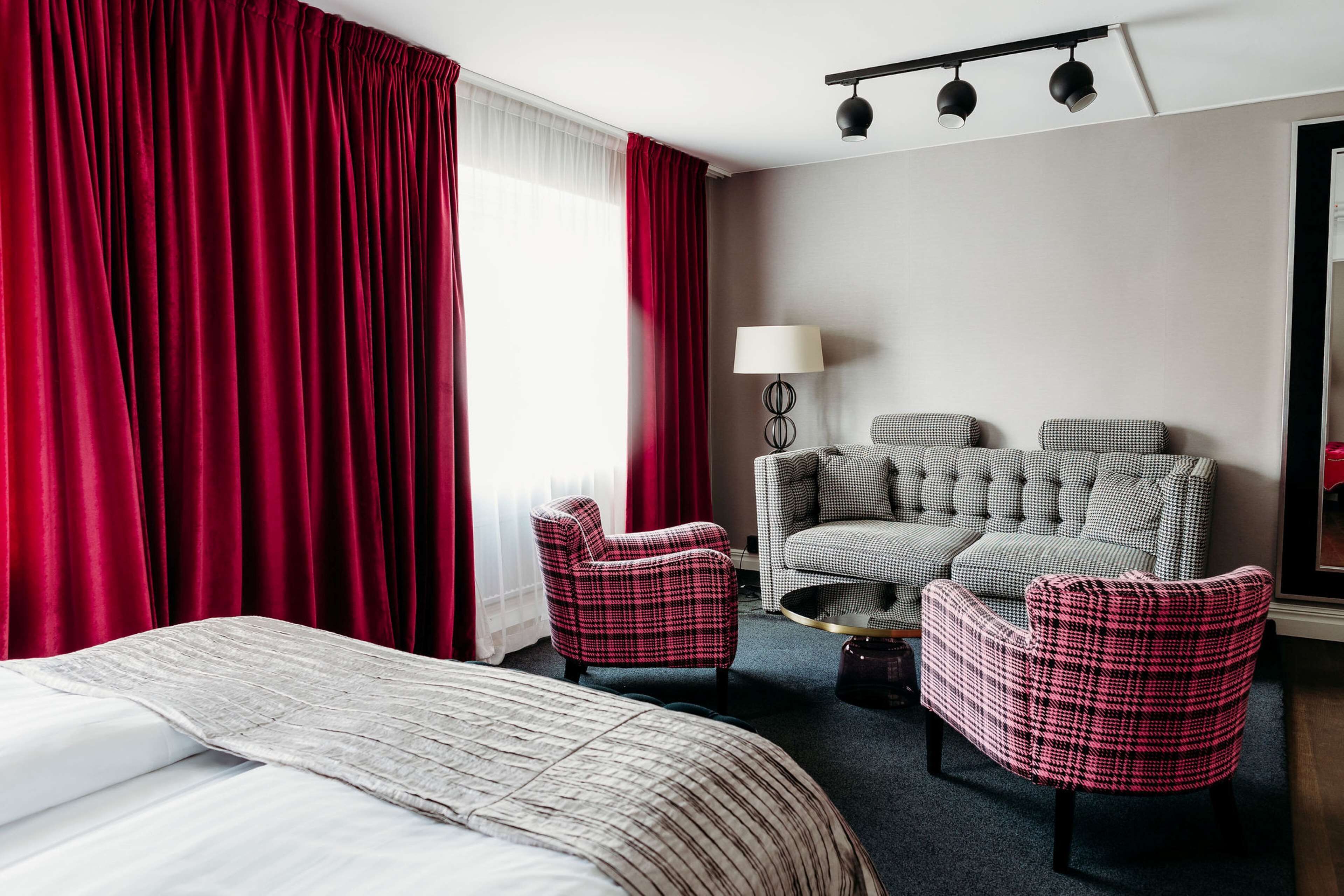 Ein Hotelzimmer mit einem Bett, zwei Sesseln, einem Sofa, einer Lampe und einem großen Spiegel.