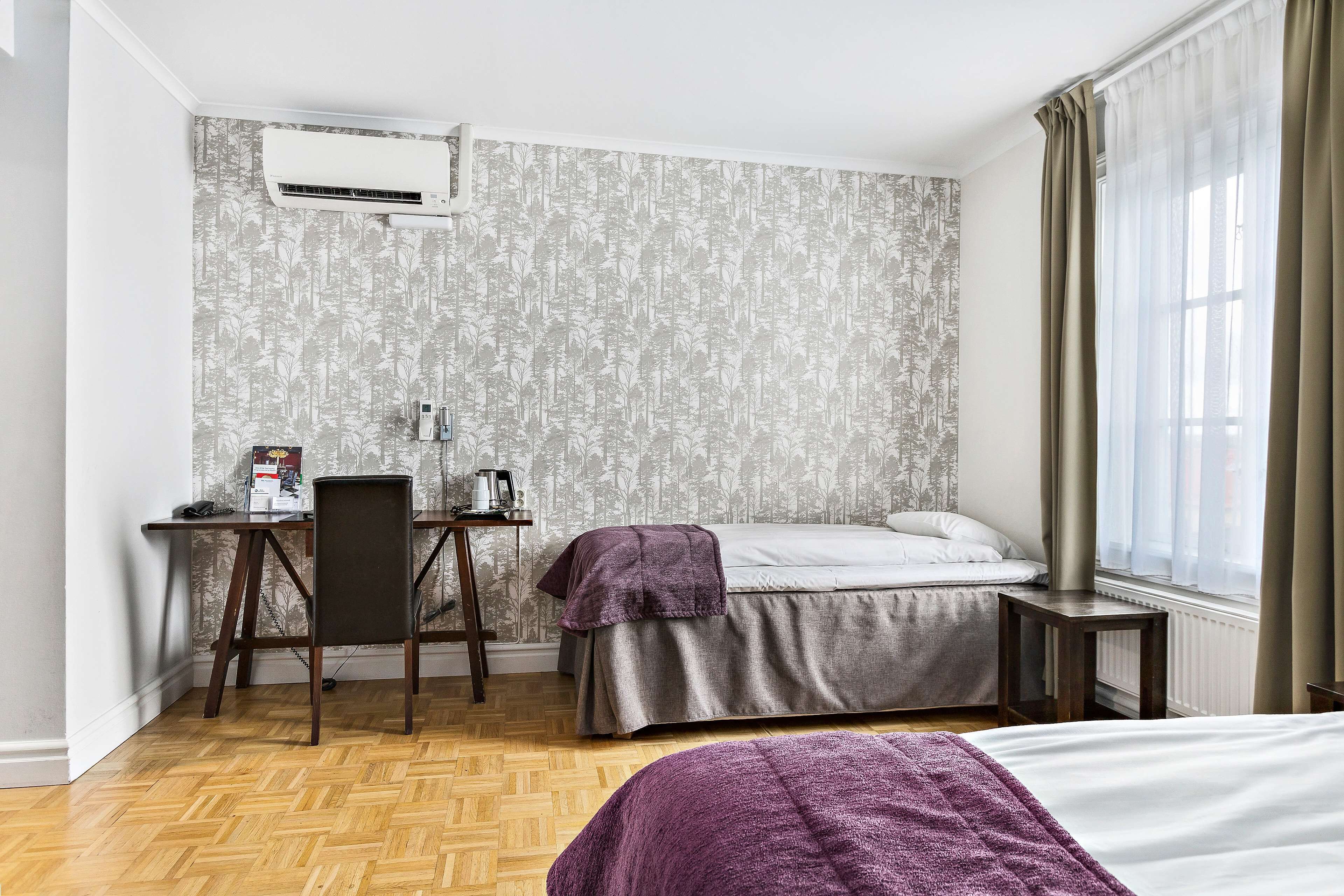 Una habitación de hotel con cama, escritorio, silla, una mesita y ventana con cortinas.