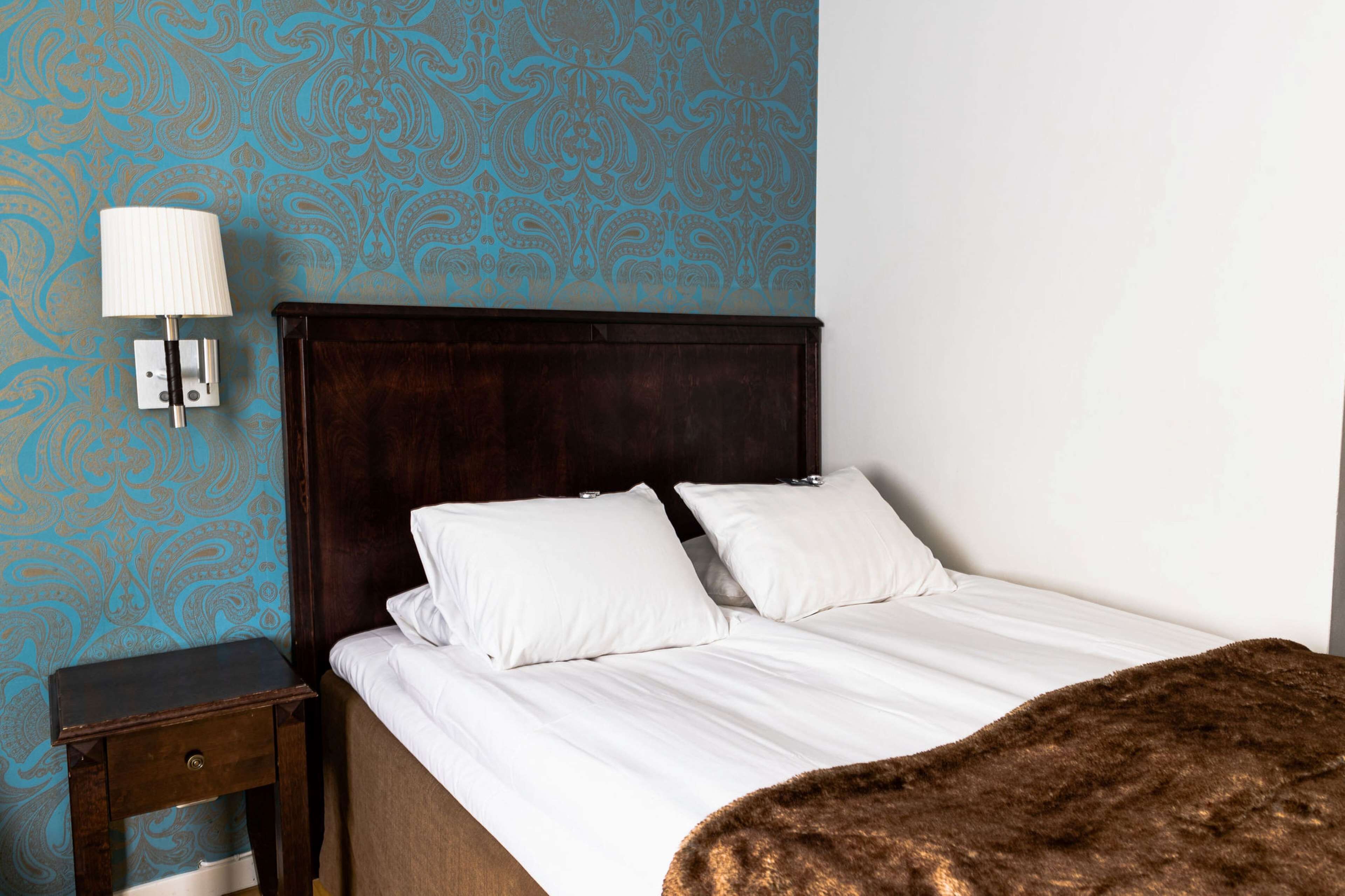 A bedroom with a wooden headboard, white bedding, and a patterned blue wall.