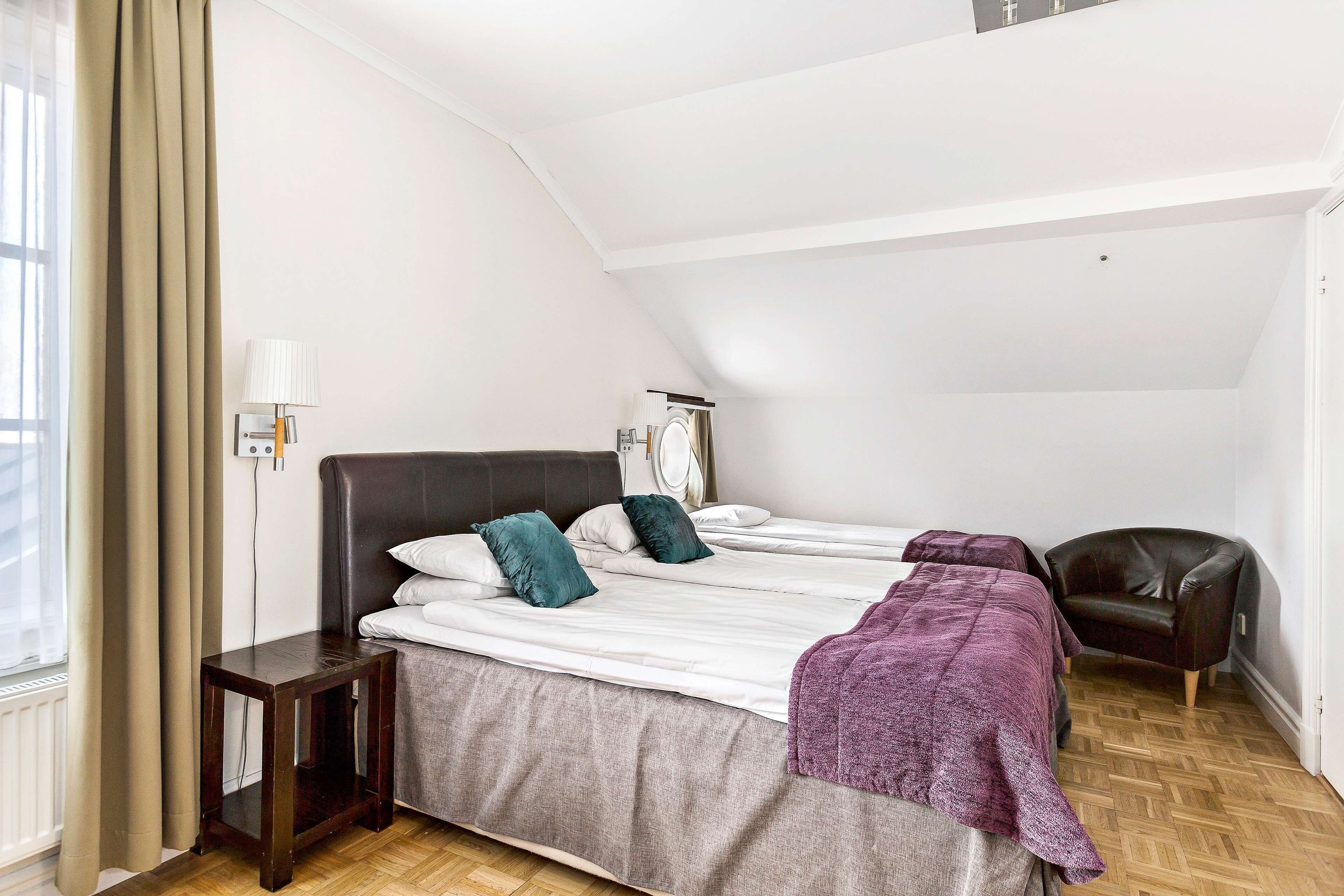 Un dormitorio con cama, una silla, una mesita de noche y una ventana con cortinas.