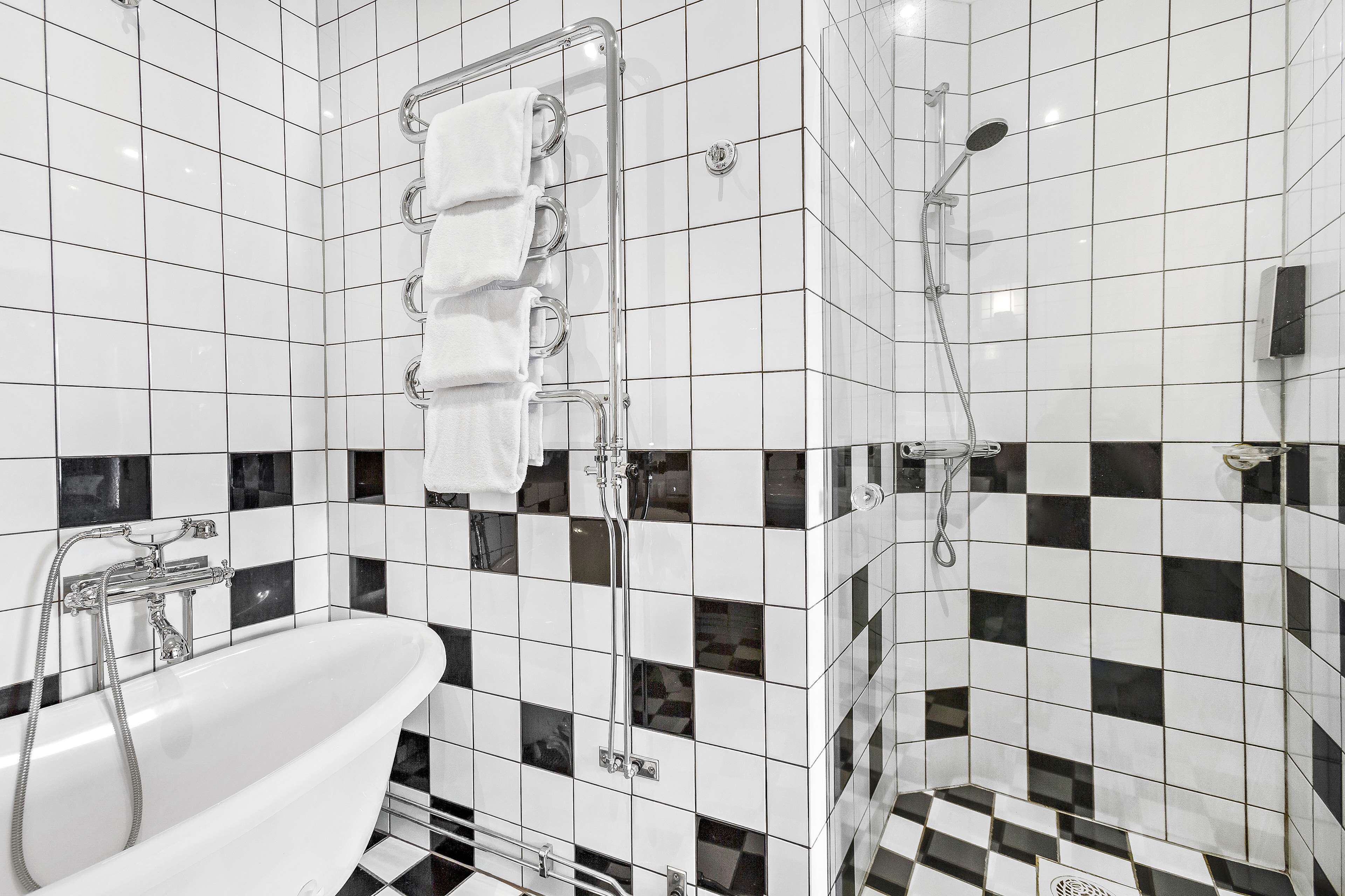 A bathroom with a freestanding bathtub, a glass shower enclosure, and black and white checkered tiles.