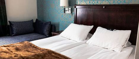 Habitación de hotel con una cama grande, un sofá más pequeño, una lámpara y un papel tapiz estampado.