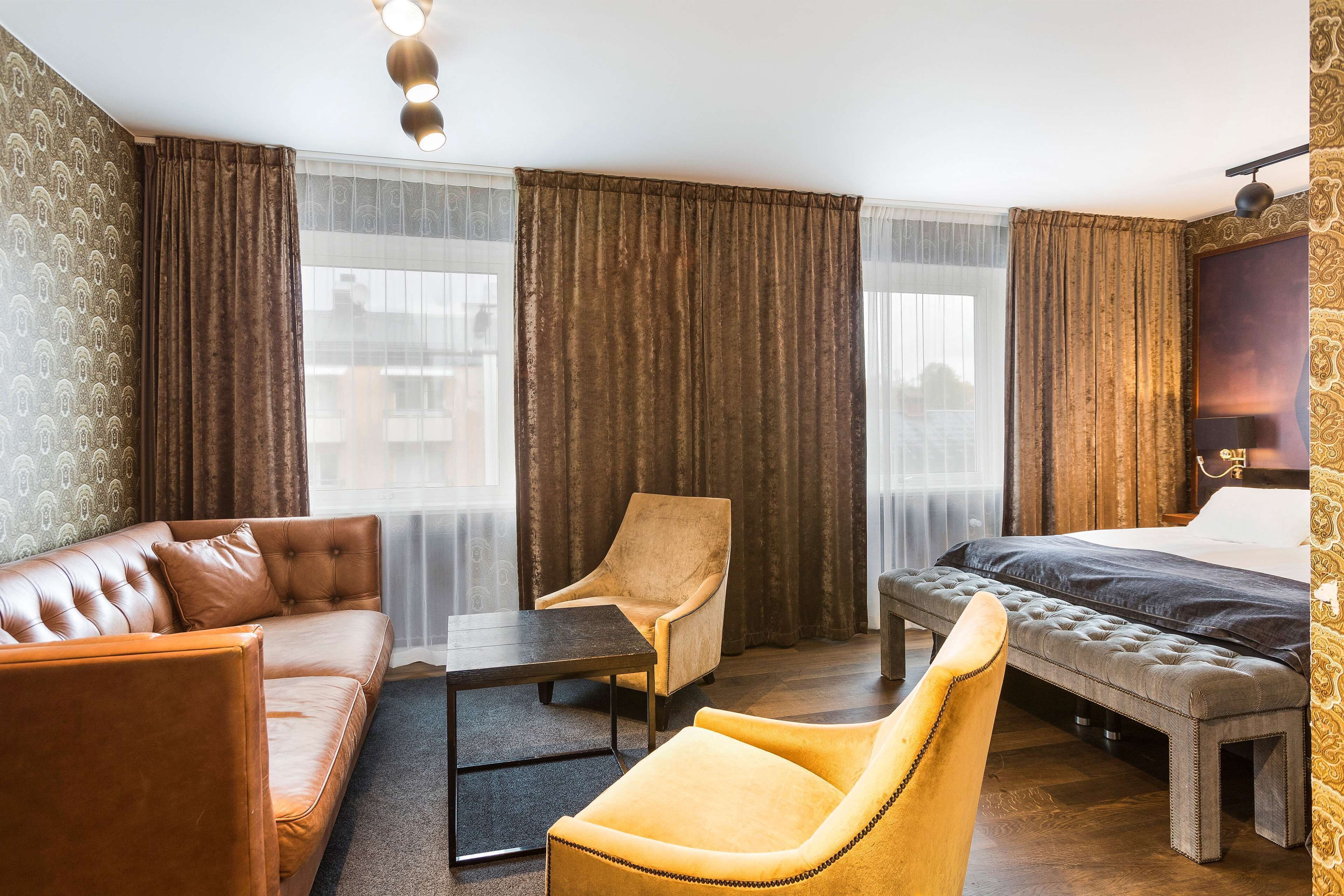 Een hotelkamer met een bank, fauteuil, bed en een kleine tafel.