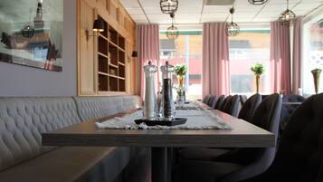 Un restaurante con una larga mesa de madera, asientos acolchados, lámparas colgantes y vistas amplias a través de grandes ventanales.