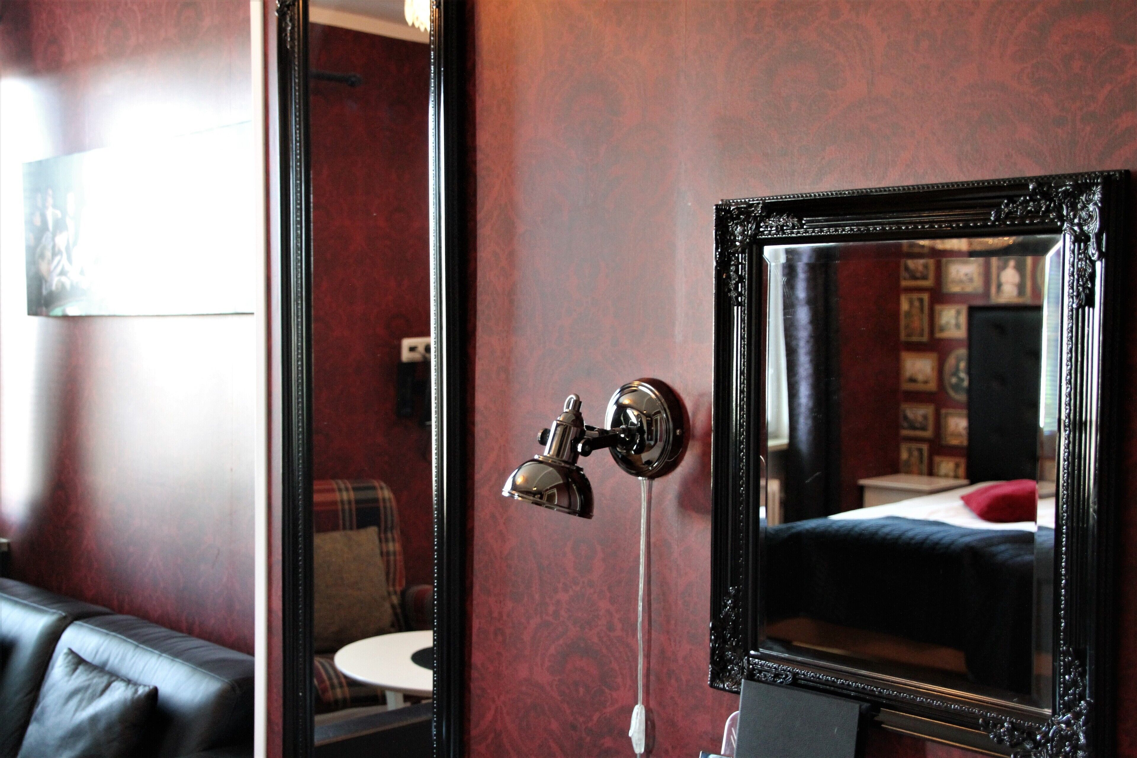 Une pièce avec un grand miroir, un luminaire fixé au mur et un lit avec un oreiller rouge.