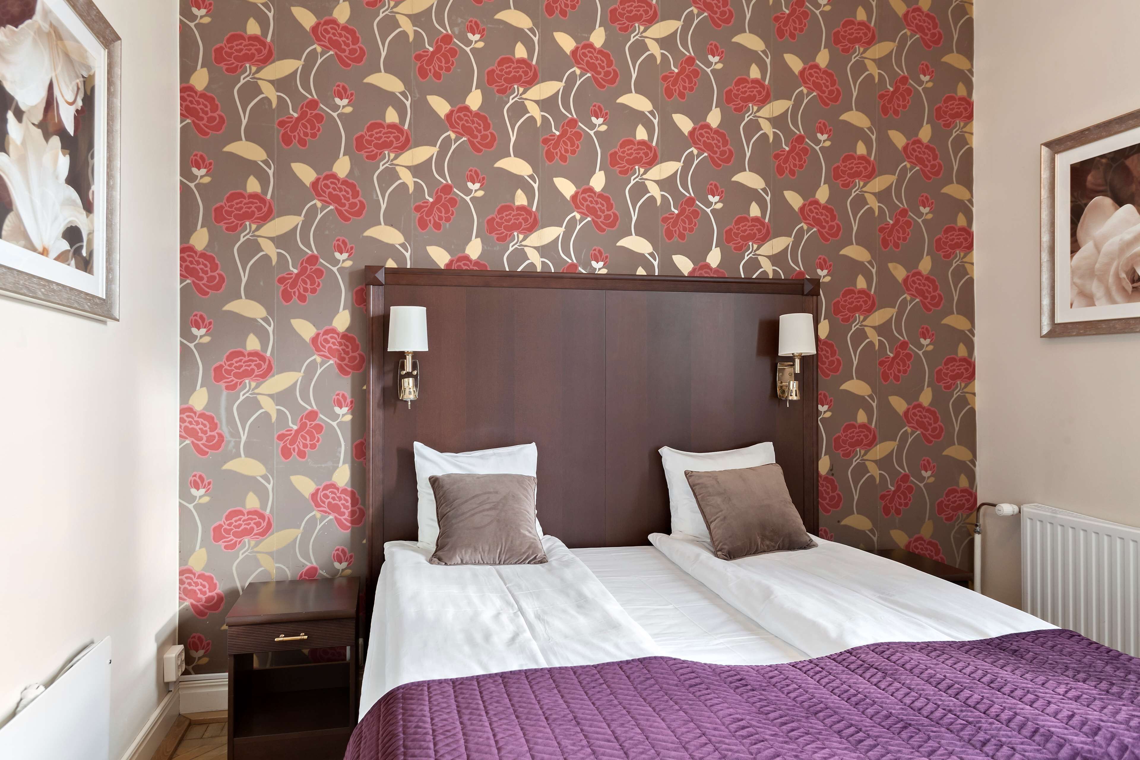 Una cama bien hecha con colcha morada, cabecera de madera y dos lámparas fijadas a la pared.